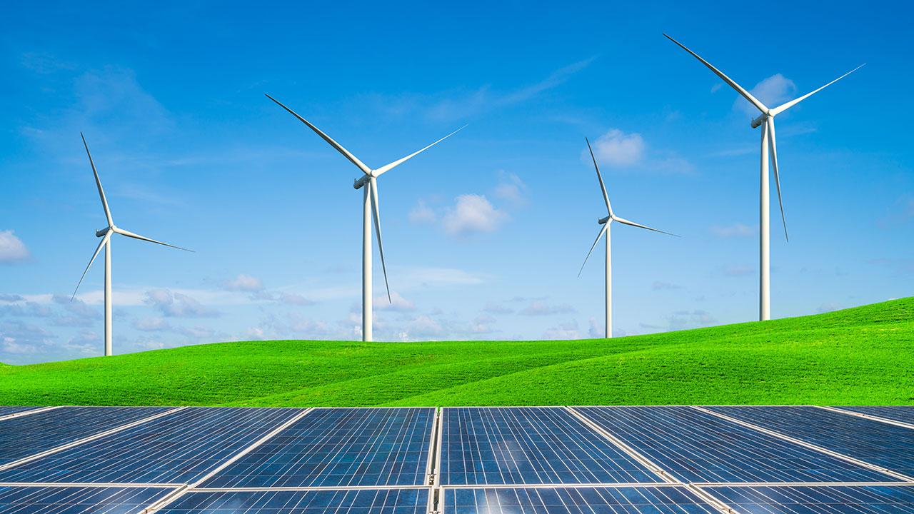 Four wind turbines on a grassy hill behind an array of solar panels