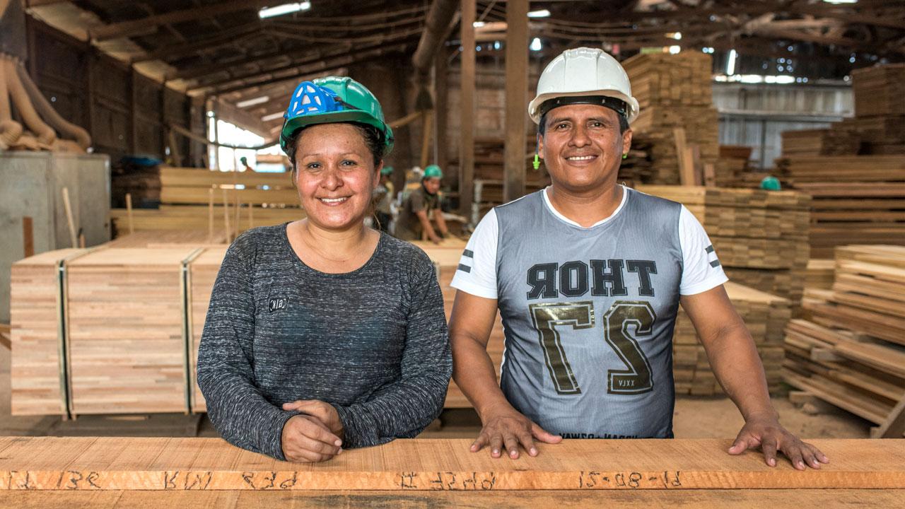 A woman and man stand in front of sustainably produced lumber as part of the Tetra Tech-led forestry program in Peru